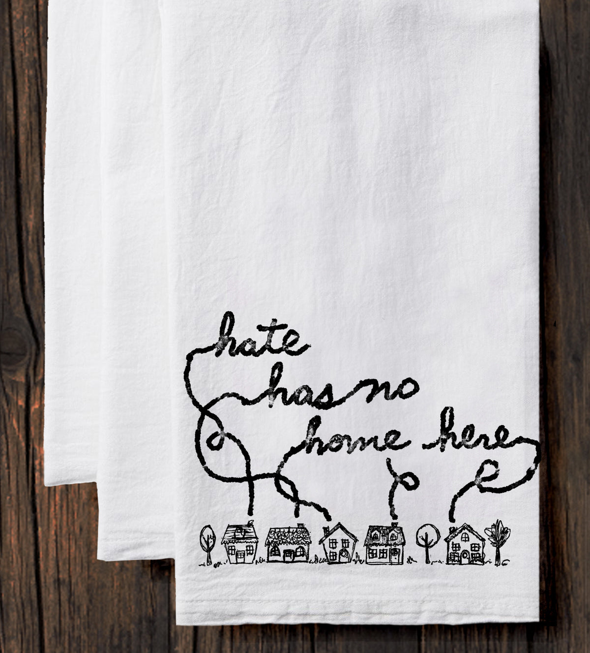 A white towel with a black handwritten text and a small illustration of houses on it.