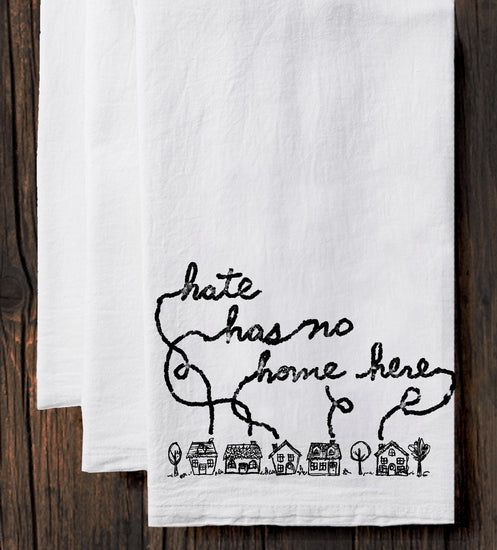 A white towel with a black handwritten text and a small illustration of houses on it.