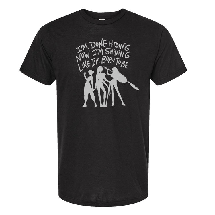A black t-shirt with a white graphic design depicting three silhouetted figures, along with the text "I'm done hiding now I'm shining like I'm born to be" printed on it.