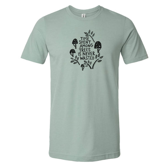 A light green t-shirt with a graphic design featuring a mushroom and leaves, along with the text "I spent among trees is never wasted".