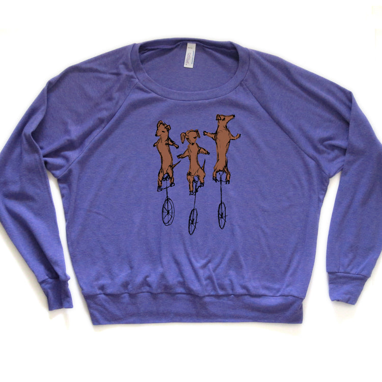 A purple long-sleeved shirt with a graphic design depicting three brown dogs riding on unicycle wheels.