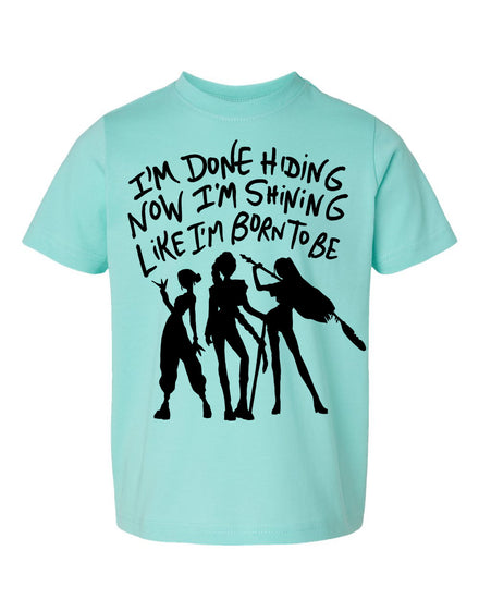 A light blue t-shirt with a graphic design featuring silhouettes of three people and text that reads "I'm done hiding now I'm shining like I'm born to be".
