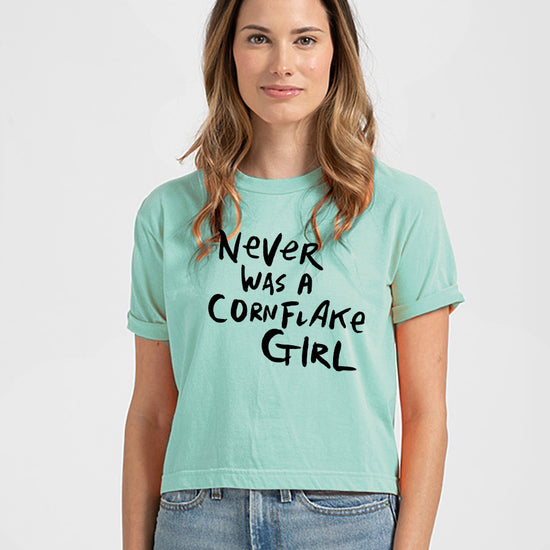 A woman wearing a mint green crop top with the text "Never was a cornflake girl" printed on it.