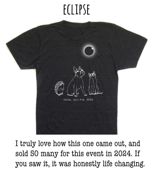 The image is a black t-shirt with a graphic design depicting a total eclipse, featuring a moon and three animals - a dog, a cat, and a hedgehog - against a dark background.