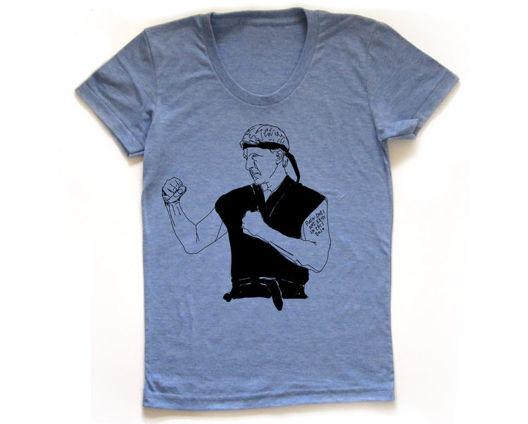 A blue t-shirt with a black and white illustration of a person in a fighting stance, wearing a bandana and a belt.
