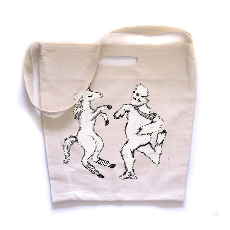 a white tote bag with a black and white illustration of a unicorn and a bear dancing together.