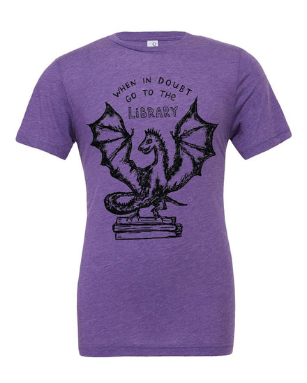 A purple t-shirt with a graphic design depicting a dragon holding a book, accompanied by the text "WHEN IN DOUBT GO TO THE LIBRARY".