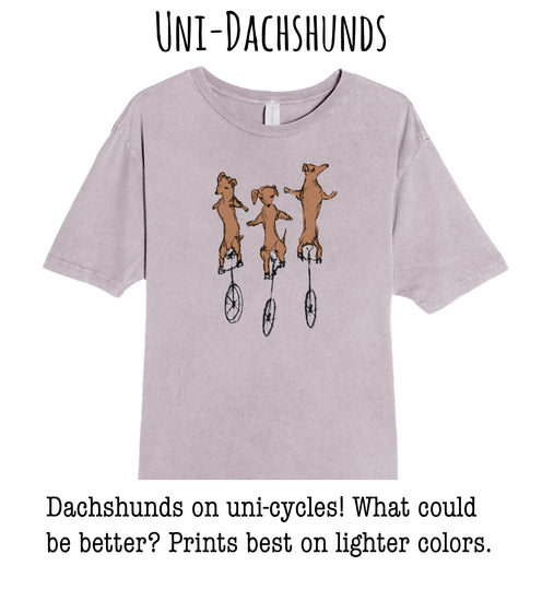 A t-shirt with a graphic design of three dachshunds riding on unicycle wheels.