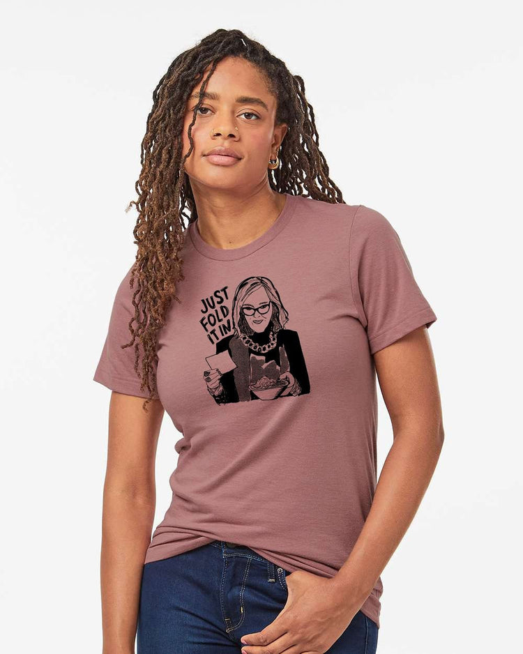 A woman with dreadlocks wearing a pink t-shirt with a graphic design and text printed on it.