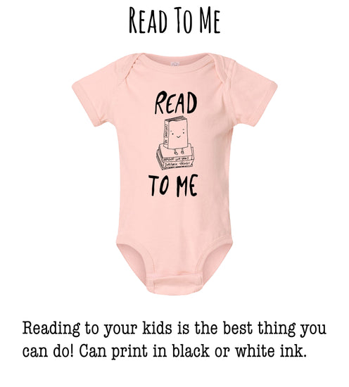 A pink onesie with the text "READ TO ME" printed on it, along with a small illustration of a book.