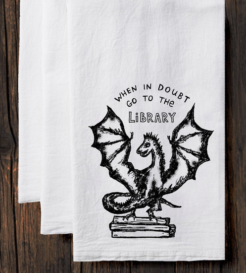 A white towel with a black illustration of a dragon and the text "WHEN IN DOUBT GO TO THE LIBRARY" printed on it.