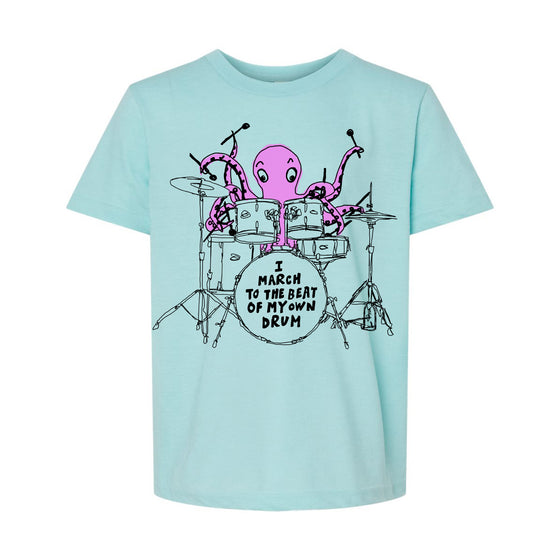 A light blue t-shirt with a graphic design depicting an octopus playing a drum set and the text "I march to the beat of my own drum" printed on it.