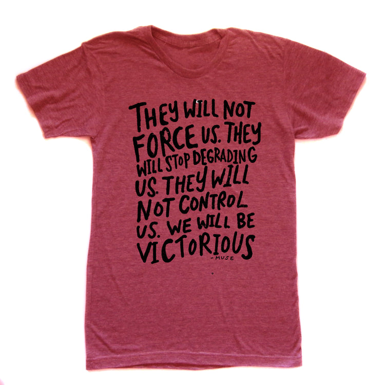 a red t-shirt with a black text design printed on it. The text reads: "They will not force us. They will stop degrading us. They will not control us. We will be victorious."