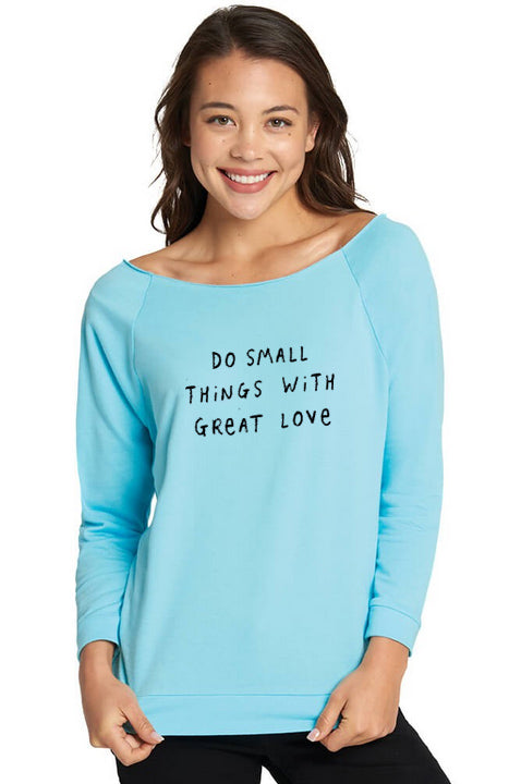 A woman wearing a light blue long-sleeved shirt with the text "Do small things with great love" printed on it.