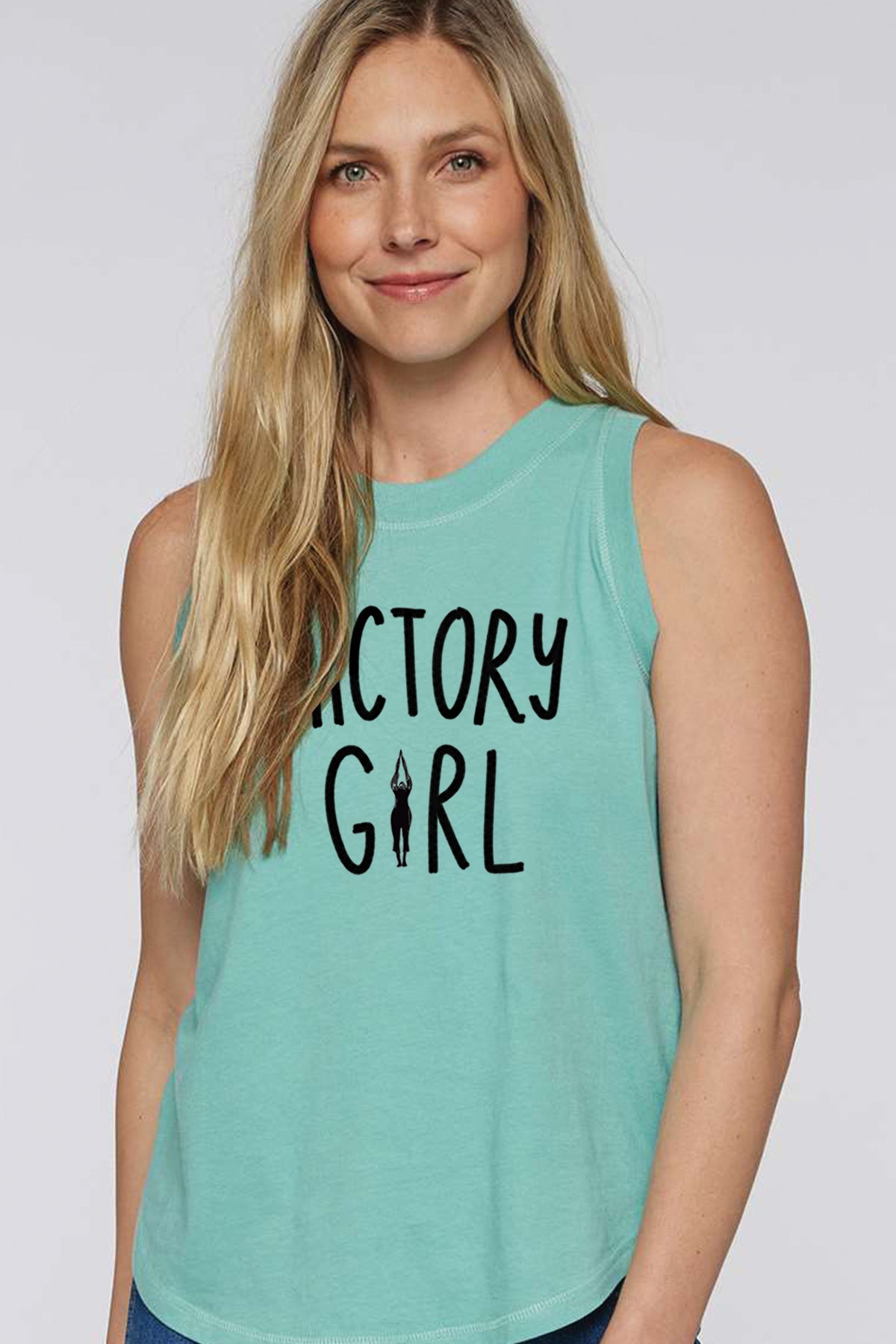 A smiling woman with long blonde hair wearing a turquoise tank top with the text "ACTORY GIRL" printed on it.