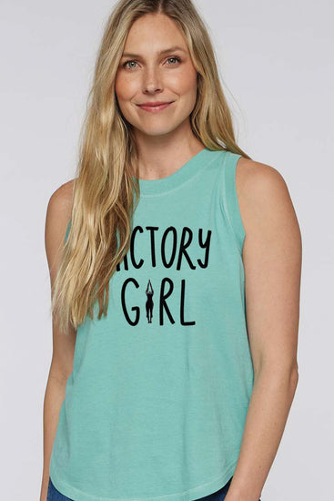 A smiling woman with long blonde hair wearing a turquoise tank top with the text "ACTORY GIRL" printed on it.