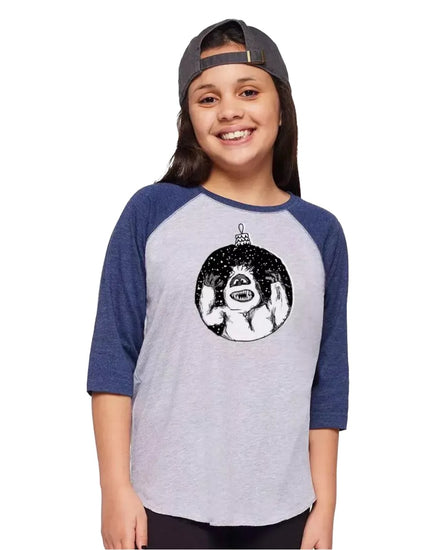 A young girl wearing a baseball cap and a t-shirt with a graphic of a monster smiling.