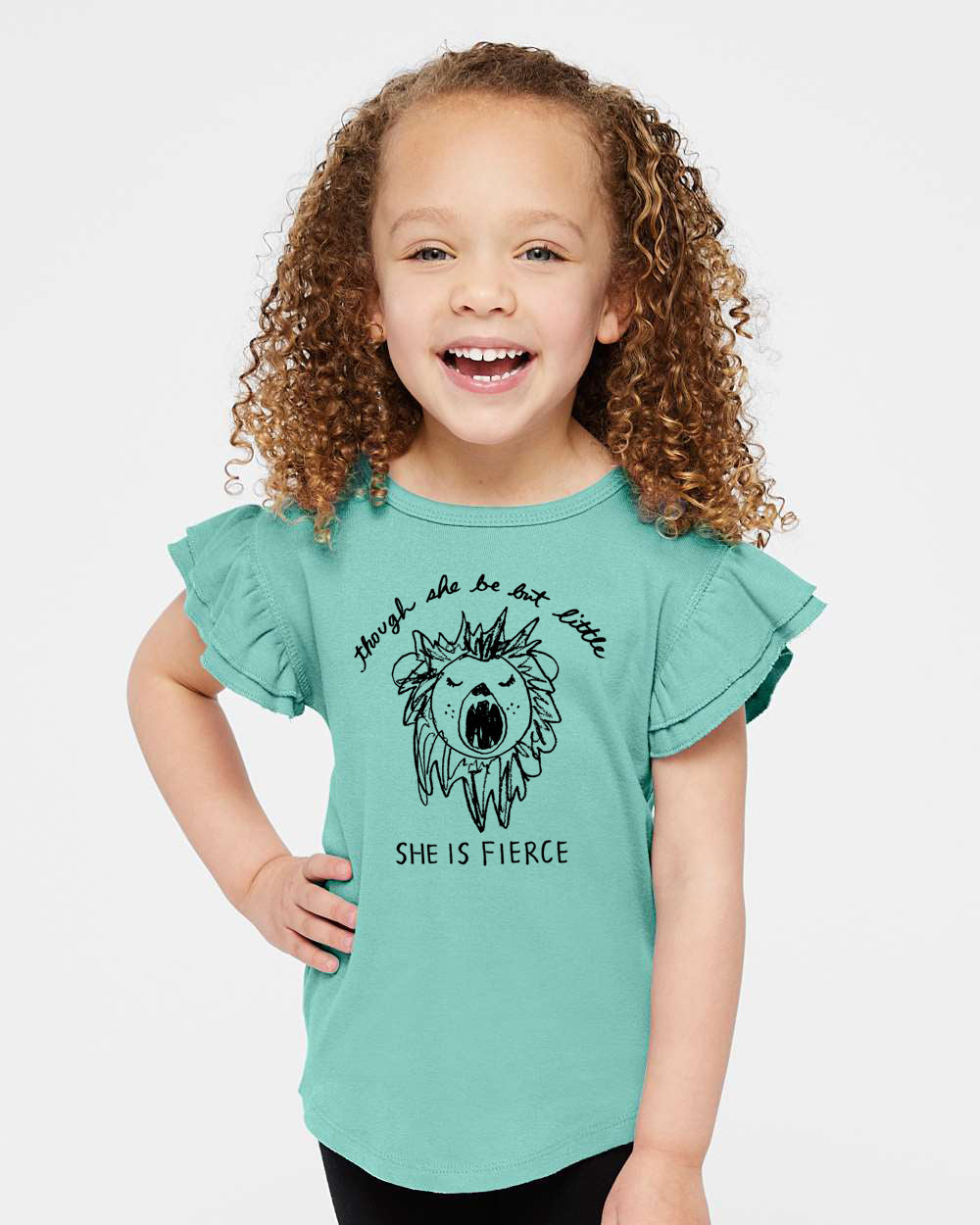 A young girl with curly hair is smiling and wearing a teal-colored t-shirt with a lion graphic and the text "She is fierce".