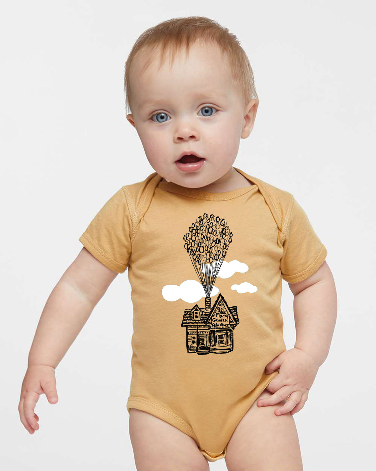 A baby wearing a yellow onesie with a graphic of a house and balloons floating above it.