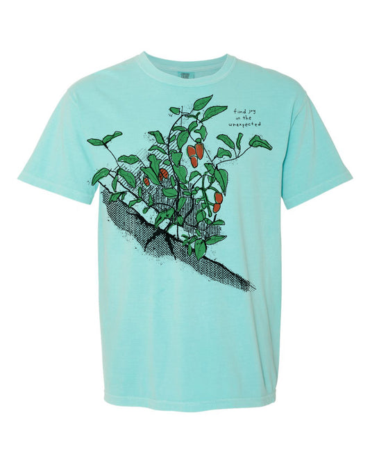 A light blue t-shirt with a graphic design depicting a plant with green leaves and orange fruits.