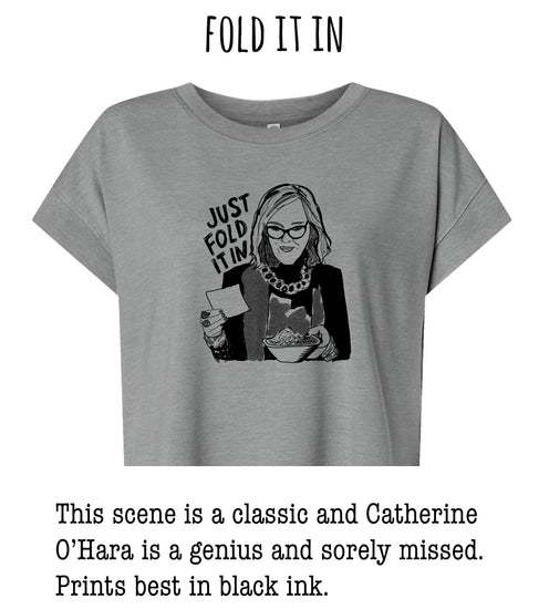 This image depicts a woman wearing glasses and holding a bowl of cereal, with the text "Just fold it in" above her. The scene is described as a classic and Catherine O'Hara is a Genius and Sorely Missed. The image is described as a classic and Catherine O'Hara is a Genius and Sorely Missed. Prints best in black ink.