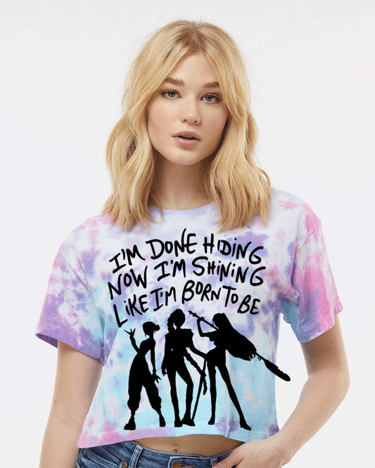 A young woman with blonde hair wearing a tie-dye shirt with a graphic design and text printed on it.