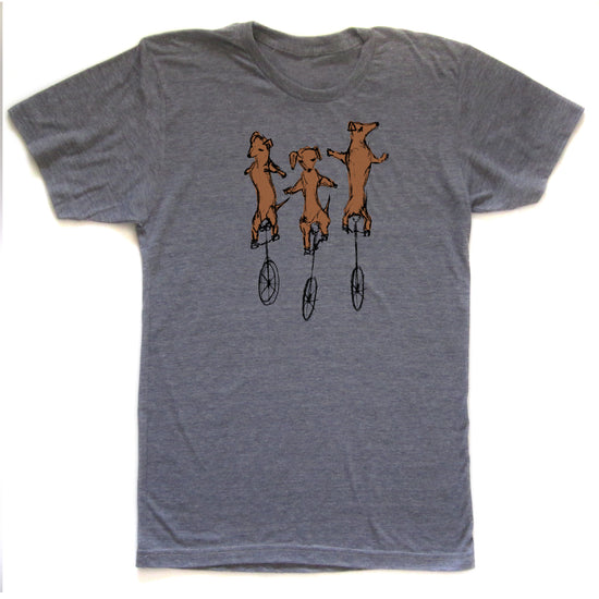 A gray t-shirt with a graphic design depicting three brown dogs riding on unicycle wheels.