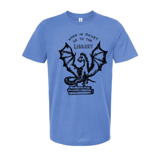 A blue t-shirt with a graphic design depicting a dragon standing on a stack of books, accompanied by the text "WHEN IN DOUBT GO TO THE LIBRARY".