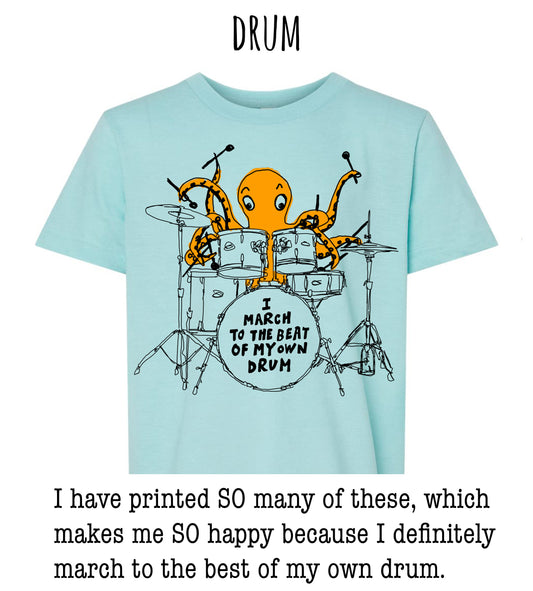 an orange octopus playing a drum set, with the text "I MARCH TO THE BEAT OF MY OWN DRUM" printed on the t-shirt.