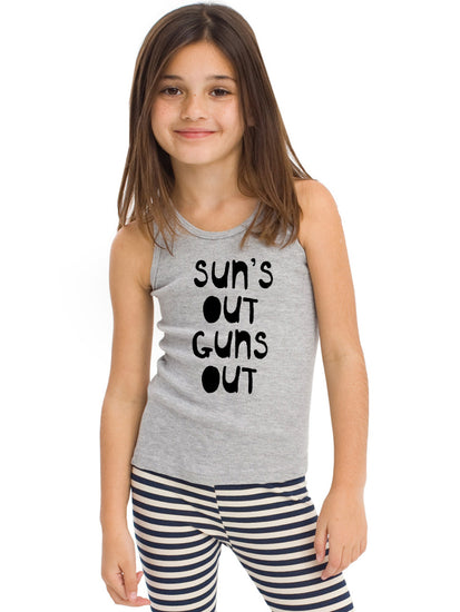 A young girl with long brown hair is smiling and wearing a gray tank top with the text "SUN'S OUT GUNS OUT" printed on it.