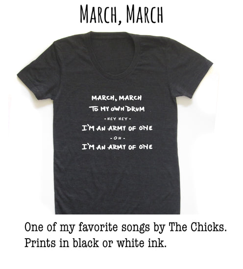 A black t-shirt with white text that reads "March, March to my own drum - Hey, I'm an army of one - Oh, I'm an army of one" printed on it.