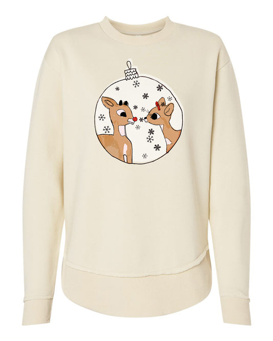 A cream-colored sweater with a circular graphic design featuring two cartoon reindeer, one with a red bow, surrounded by snowflakes.