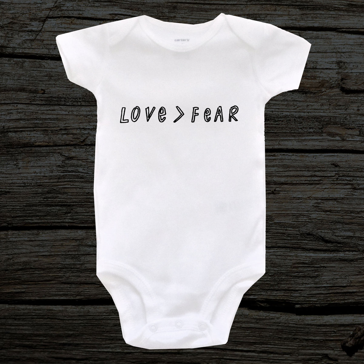 A white baby onesie with the text "LOVE > FEAR" printed on it.