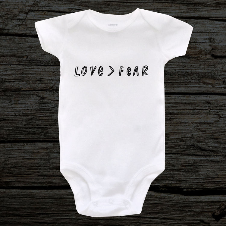 A white baby onesie with the text "LOVE > FEAR" printed on it.