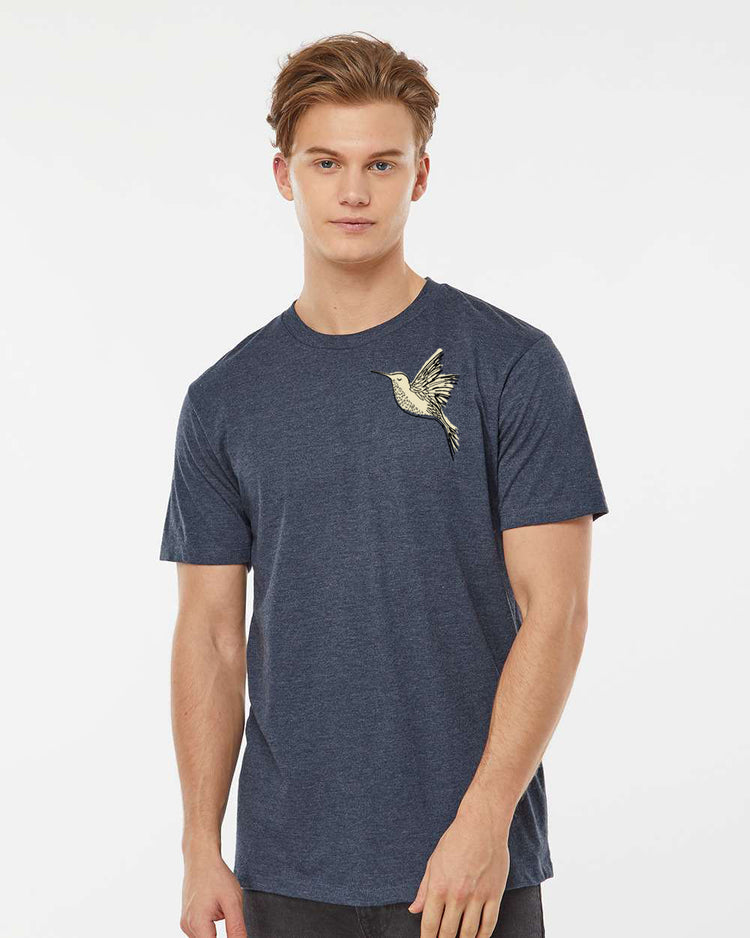 A young man wearing a blue t-shirt with a bird embroidered on it, posing for a portrait against a white background.