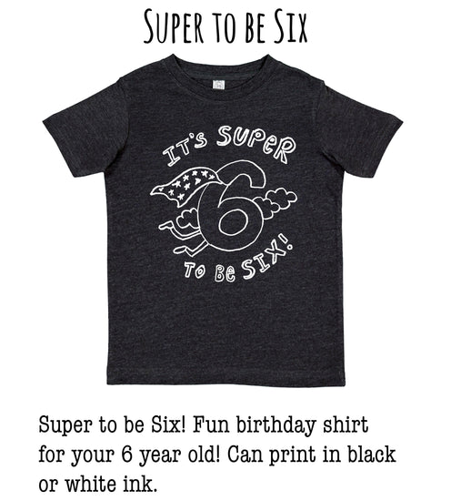 A black t-shirt with a white graphic design that says "It's SUPER to be Six" and features a number 6 with clouds and lightning bolts.