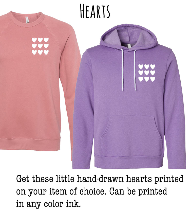 two sweatshirts with a heart design on the front. The sweatshirt on the left is pink, while the sweatshirt on the right is purple. The text suggests that the sweatshirts can be printed with hand-drawn hearts in any color ink, and that the choice of color is up to the individual.