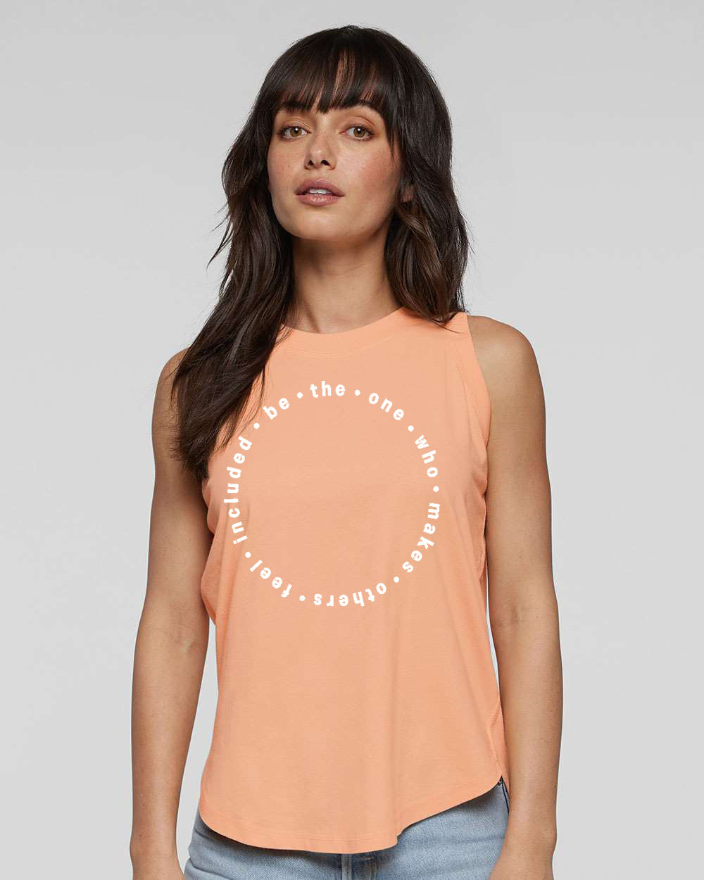 A woman with long dark hair wearing a peach-colored sleeveless top with a circular design on it.