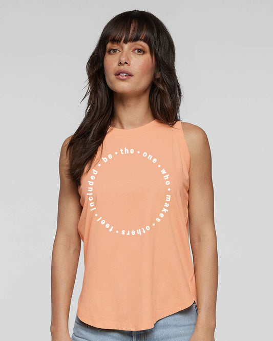 A woman with long dark hair wearing a peach-colored sleeveless top with a circular design on it.