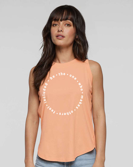 A woman with long dark hair wearing a peach-colored sleeveless top with a circular design on it.