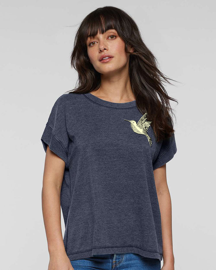 A woman with long dark hair wearing a gray t-shirt with a yellow bird design on the front.