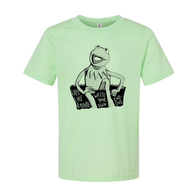 A light green t-shirt with a black and white illustration of Kermit the Frog sitting on a rock and the text "Lives like a movie, write your own" printed on it.