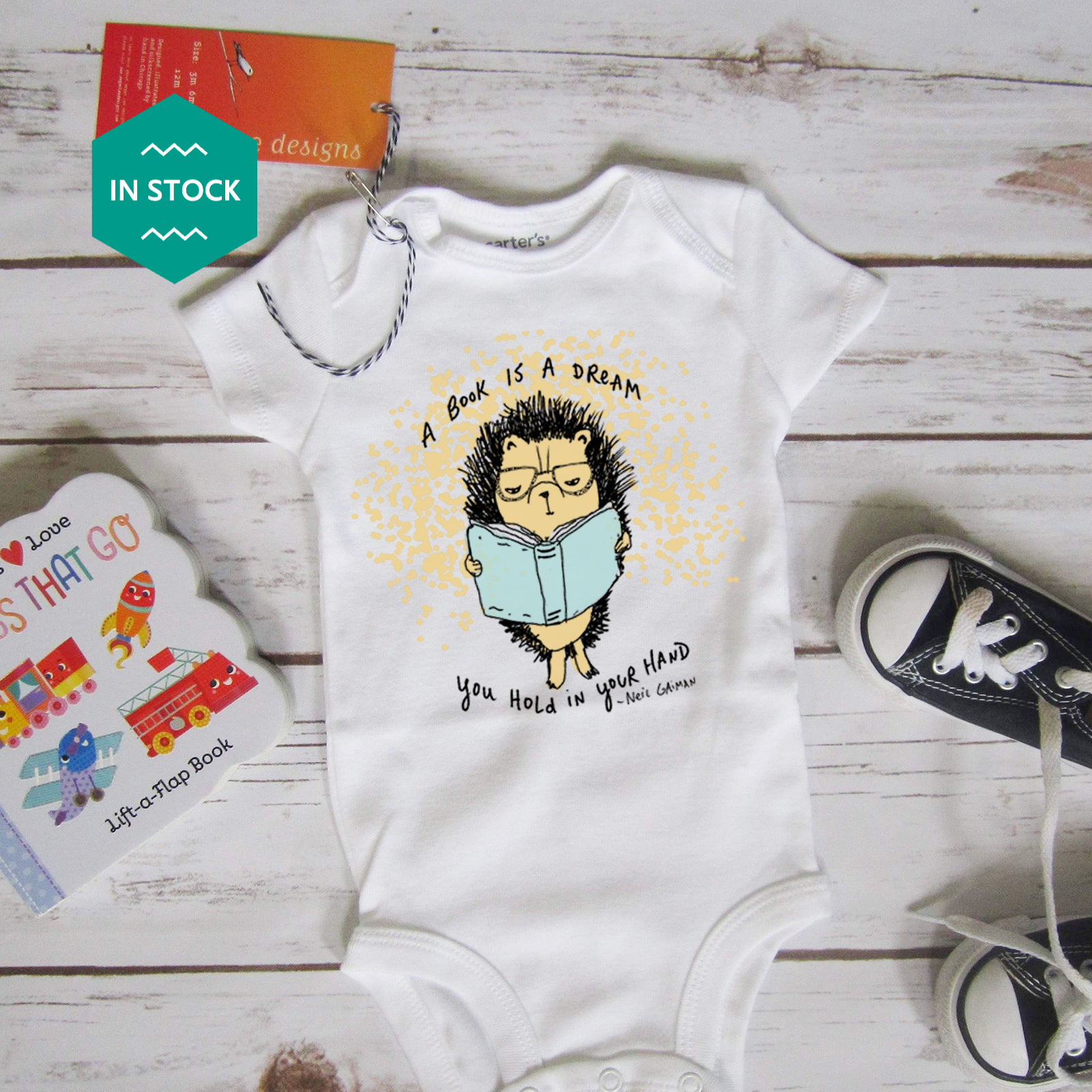 a baby bodysuit with a picture of a hedge reading a book