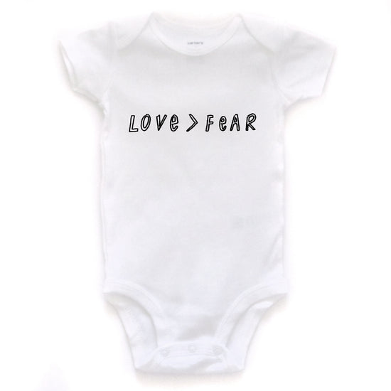 A white baby onesie with the text "LOVE > FEAR" printed on it.