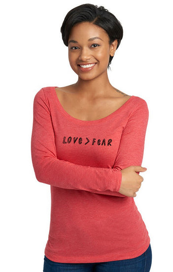 A smiling woman wearing a red long-sleeved shirt with the text "LOVE > FEAR" printed on it.