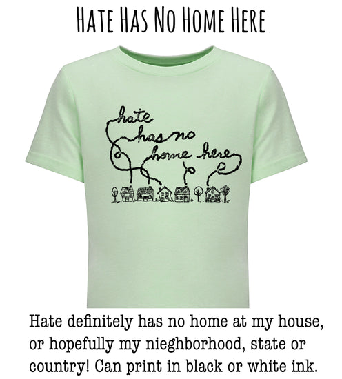 A light green t-shirt with a black handwritten message that reads " Hate has no home here" and a small illustration of houses below the text.