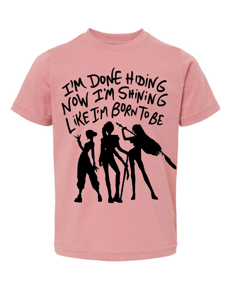 A pink t-shirt with a graphic design featuring silhouettes of three people and text that reads "I'm done hiding now I'm shining like I'm born to be".