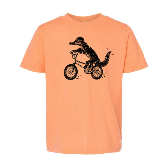 a t-shirt with a graphic of a crocodile riding a bicycle.