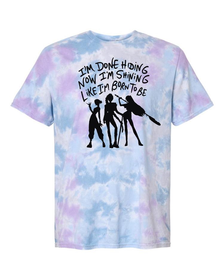 A tie-dye t-shirt with a graphic design featuring silhouettes of three people and text that reads "I'm done hiding now I'm shining like I'm born to be".
