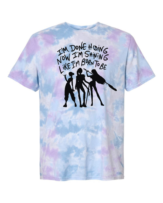 A tie-dye t-shirt with a graphic design featuring silhouettes of three people and text that reads "I'm done hiding now I'm shining like I'm born to be".